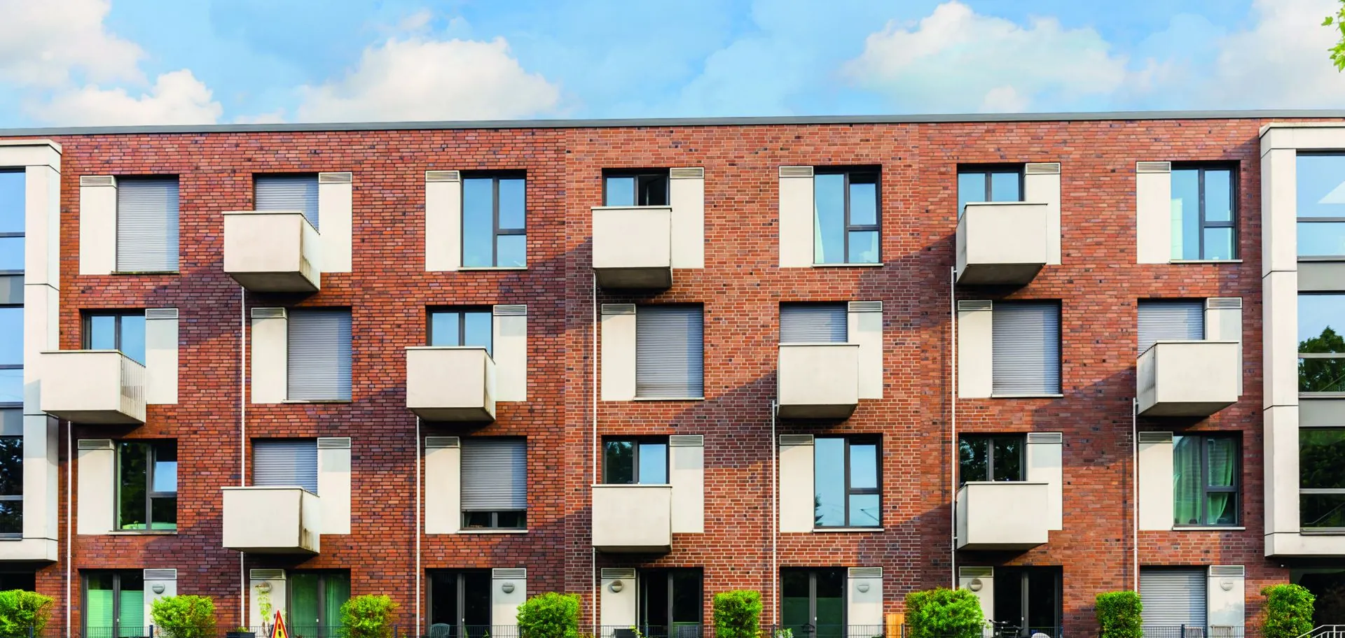 Klinkerfassade des N19 mit weißen Balkonen und begrüntem Vorgarten